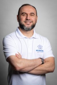 Ein Mann im weißen Polo-Shirt mit Logo des AS Pflegedienstes steht mit verschränkten Armen und lächelt freundlich in die Kamera.